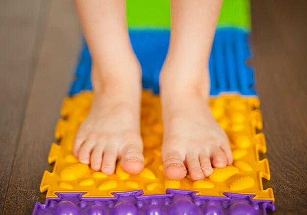 Petit garçon enfant marchant sur un tapis de massage orthopédique. Traitement et prévention des pieds plats chez les enfants.