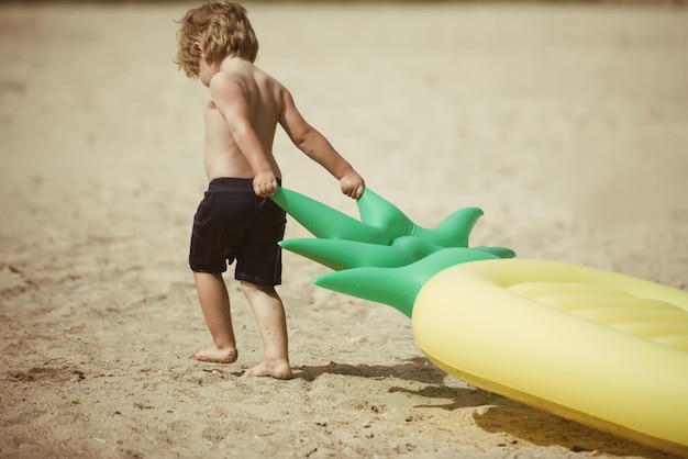 Petit garçon enfant tirer matelas pneumatique sur le sable Vacances d'été et voyage vers l'océan Activité et joie de matelas gonflable d'ananas Maldives ou Miami beach petit enfant sur la mer des Caraïbes aux Bahamas