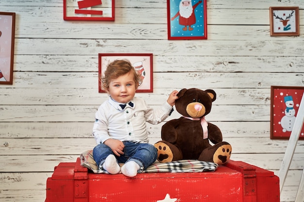Un petit garçon est assis sur un coffre à côté d'un jouet.