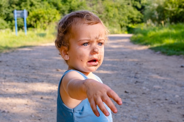 Le petit garçon étonné s'accroupit sur le visage des garçons d'herbe est enduit de saleté