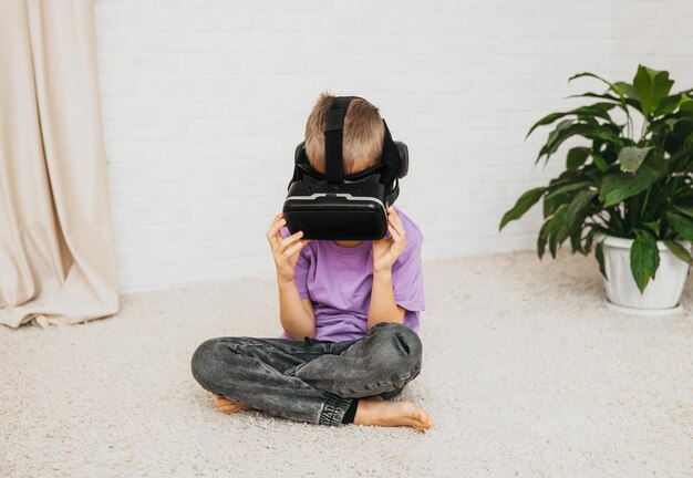 Un petit garçon excité dans des lunettes de réalité virtuelle est assis par terre à la maison.