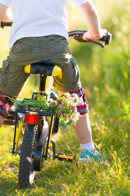 petit garçon faisant du vélo jaune sur un pré avec un bouquet de fleurs sauvages