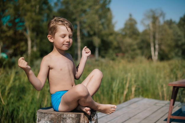 Petit garçon faisant du yoga assis sur la nature d'été de talon sur fond