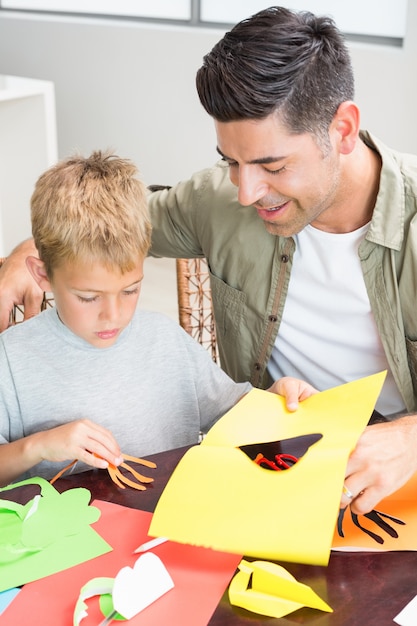 Petit garçon faisant des formes de papier avec le père à la table