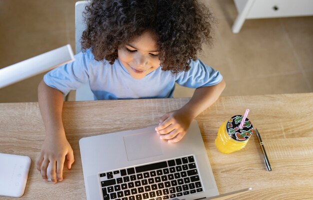 Le petit garçon fait ses devoirs à la maison avec l'ordinateur