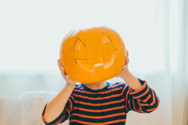 Un petit garçon fait une tête de citrouille d'halloween à la maison