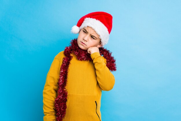 Petit garçon fête le jour de Noël avec un bonnet de Noel isolé qui se sent triste et pensif, regardant l'espace de la copie.