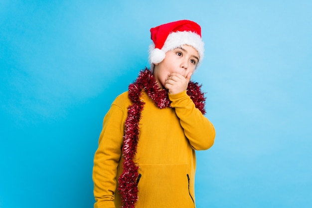 Petit garçon fête le jour de Noël portant un bonnet de Noel isolé réfléchie à la recherche d'un espace copie couvrant la bouche avec la main.
