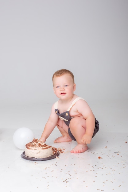 Le petit garçon fête son anniversaire avec des ballons et des gâteaux sur fond blanc