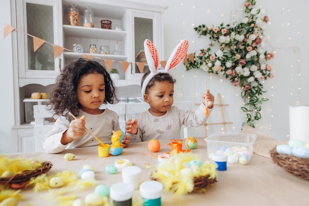 Un petit garçon et une fille afro-américains peignent des oeufs de Pâques à la maison des enfants noirs se préparent pour Pâques