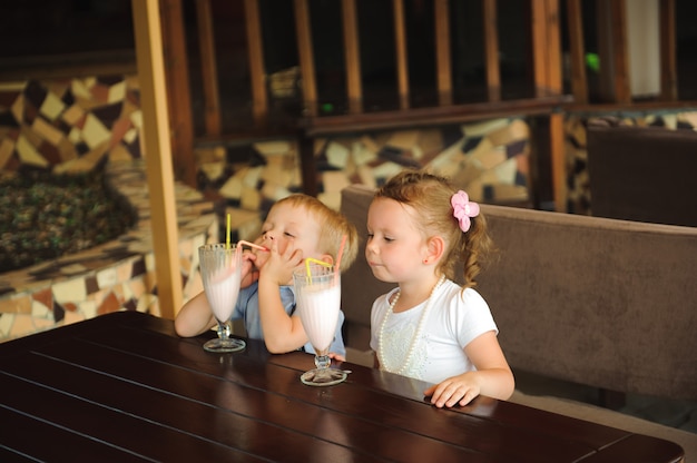 Petit garçon et fille buvant des milkshakes dans un café en plein air.