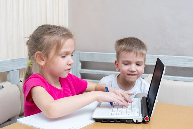 Petit garçon et fille étudient en ligne à la maison. La fille tape le texte sur l'ordinateur portable.