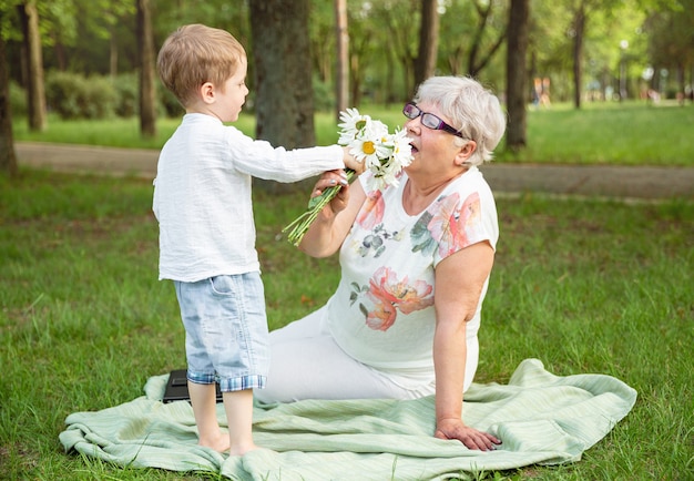 Petit garçon avec des fleurs et sa grand-mère dans le parc. Bonne fête des mères