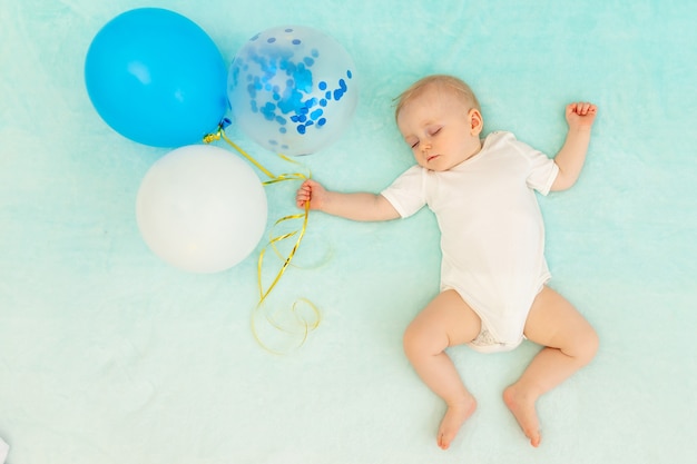 Un petit garçon sur fond bleu dort et dans un rêve volant avec des ballons