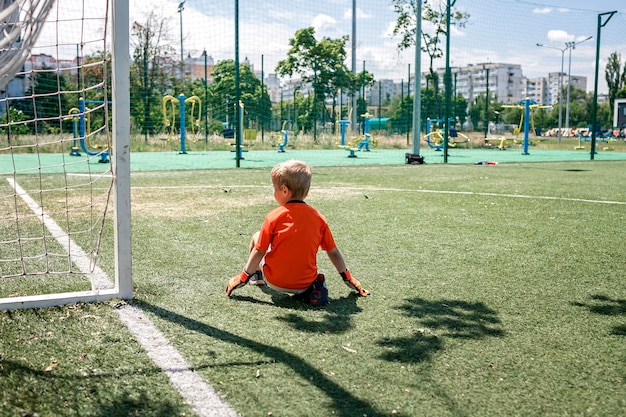 Petit garçon en forme de football noir et orange jouant au football sur un terrain ouvert dans la cour jeune gardien de but