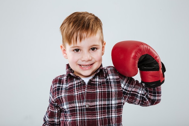 Petit garçon gai dans des gants de boxe montrant des biceps