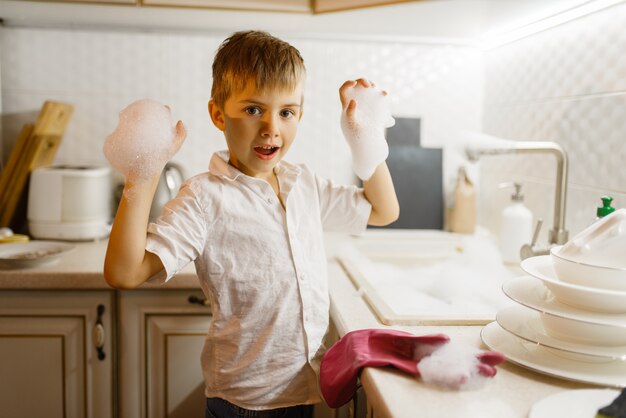 Petit garçon en gants à laver la vaisselle dans la cuisine