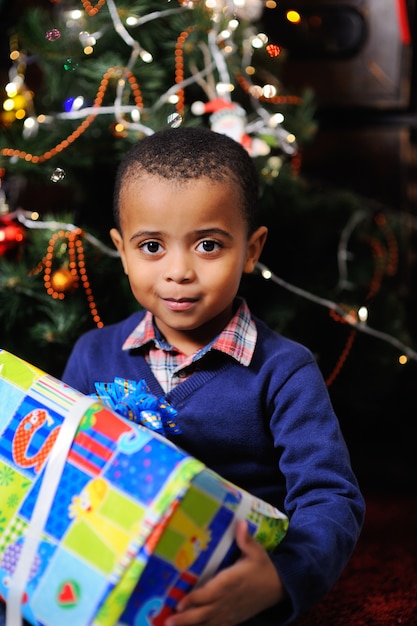 Petit garçon garçon afro-américain avec un cadeau de Noël en main sur un sapin de Noël