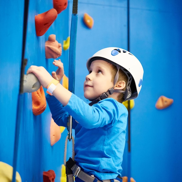 Petit garçon grimpe au parc d'attractions sur le mur bleu