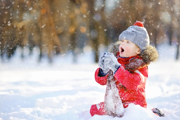 Petit garçon en habits d&#39;hiver rouge s&#39;amuser avec la neige