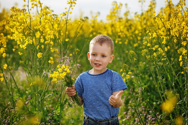 Petit garçon heureux avec un bouquet de fleurs est dans le champ de colza à fleurs jaunes