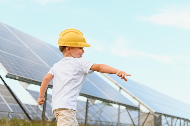 Un petit garçon heureux dans un casque jaune se tient sur une ferme de panneaux solaires