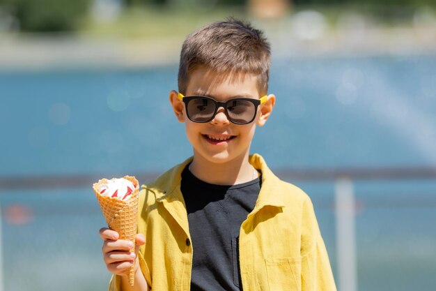 Photo un petit garçon heureux mange de la crème glacée dans un cône de gaufres en été lors d'une promenade