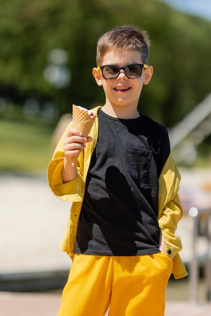 Un petit garçon heureux mange de la glace dans un cornet gaufré en été lors d'une promenade
