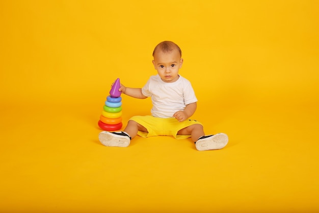 un petit garçon heureux vêtu d'un t-shirt blanc et d'un short jaune joue un jouet pyramidal