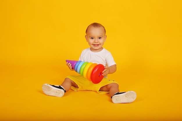 un petit garçon heureux vêtu d'un t-shirt blanc et d'un short jaune joue un jouet pyramidal