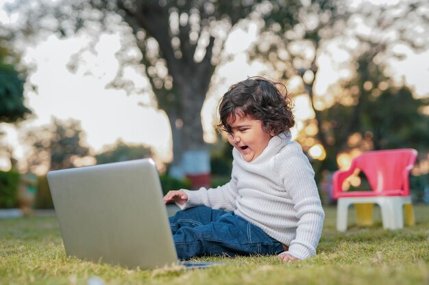 Petit garçon intelligent jouant au jardin tout en utilisant un ordinateur portable sur le concept d'assurance meadowhome