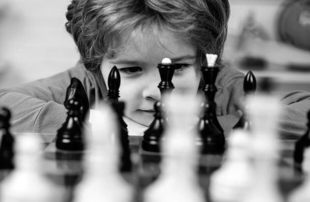 Photo petit garçon intelligent pensant aux échecs enfants développement précoce fils jouent aux échecs et sourient à la maison portrait de près visage drôle