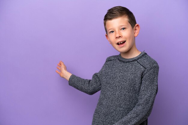 Petit garçon isolé sur fond violet tendant les mains sur le côté pour inviter à venir