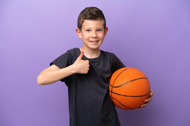 Petit garçon jouant au basket-ball isolé sur fond violet donnant un geste du pouce levé