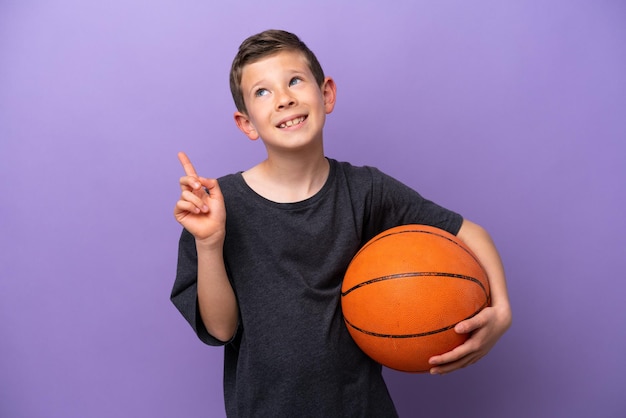 Petit garçon jouant au basketball isolé sur fond violet pointant vers le haut une excellente idée