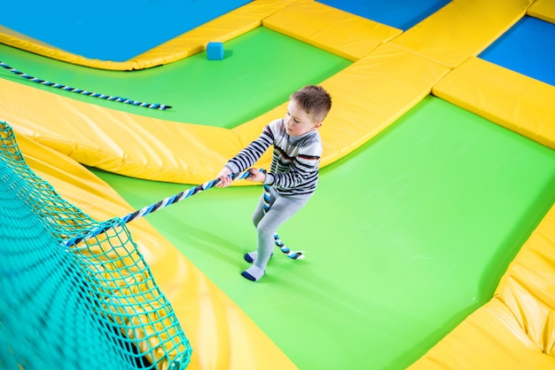 Petit garçon jouant au centre de trampoline sautant et grimpant avec une corde