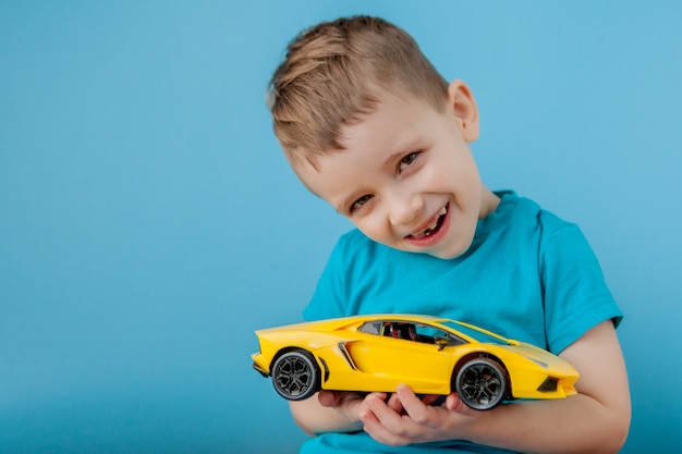 Petit garçon jouant avec une grosse voiture jaune sur mur bleu