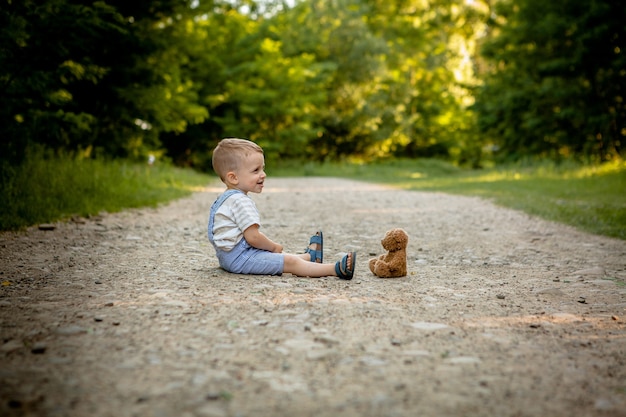 Petit garçon jouant avec un ours en peluche sur le sentier.