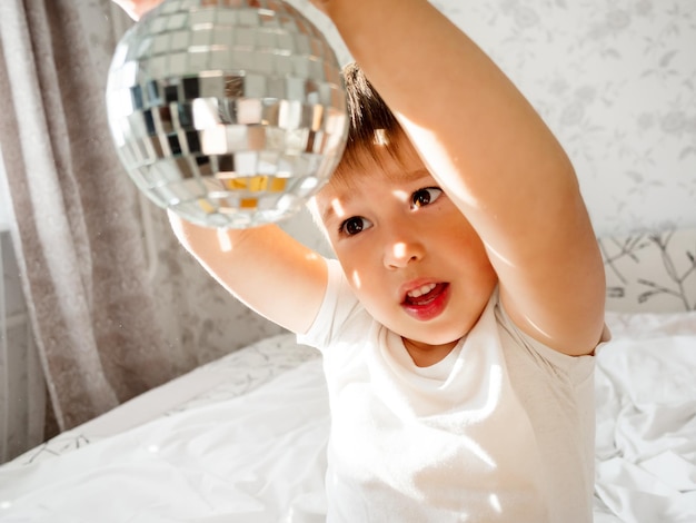 Photo petit garçon joue avec une balle de disco miroir étincelante dans le lit et rit heureux joyeux tout-petit