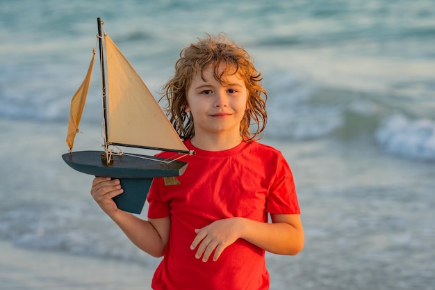 Un petit garçon joue avec un bateau jouet dans les vagues de la mer à la plage pendant les vacances d'été et