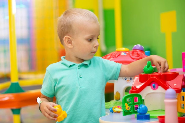 Un petit garçon joue avec beaucoup de jouets en plastique colorés à l'intérieur