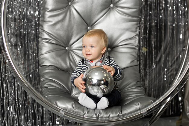 Petit garçon joue sur une chaise un bol en verre avec des boules d'argent