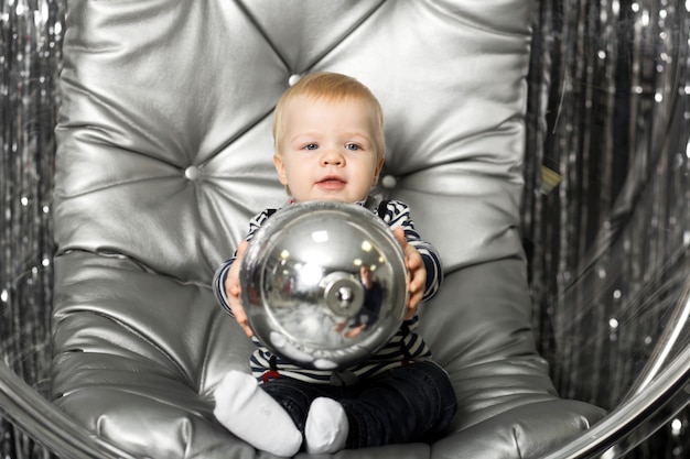 Petit garçon joue sur une chaise un bol en verre avec des boules d'argent.