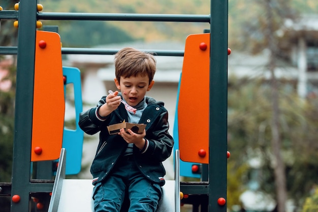 Un petit garçon joue dans le parc tout en mangeant de délicieux poffertjes frais. Mise au point sélective. Photo de haute qualité