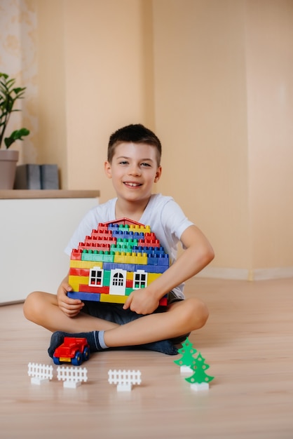 Un petit garçon joue avec un kit de construction et construit une grande maison pour toute la famille. Construction d'une maison familiale.