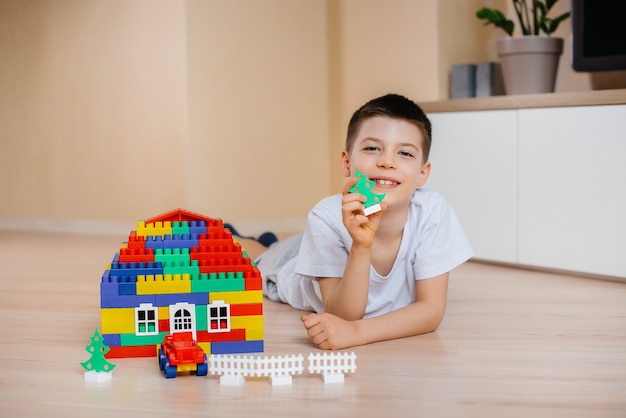 Un petit garçon joue avec un kit de construction et construit une grande maison pour toute la famille. Construction d'une maison familiale.