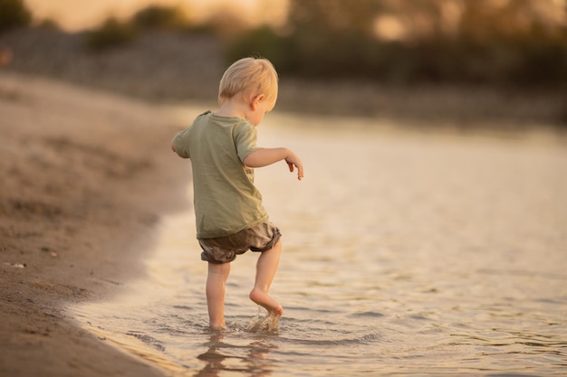 Petit garçon joue sur la rive sablonneuse de la rivière Voyage de vacances d'été Loisirs pour enfants et familles dans la nature Mer rivière été temps chaud plage de refroidissement jeux de plein air mise au point sélective