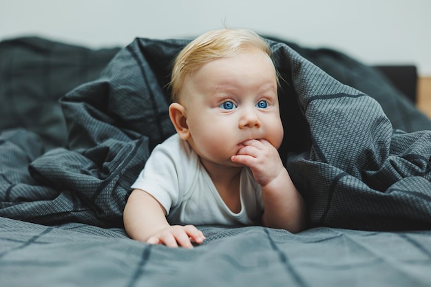 Un petit garçon joyeux avec de beaux grands yeux est allongé sur le lit à la maison dans un maillot de bain blanc sur une literie grise l'enfant est allongée sur le lit de la maison