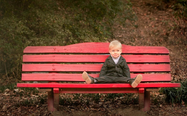 Un petit garçon joyeux sur un grand banc rouge