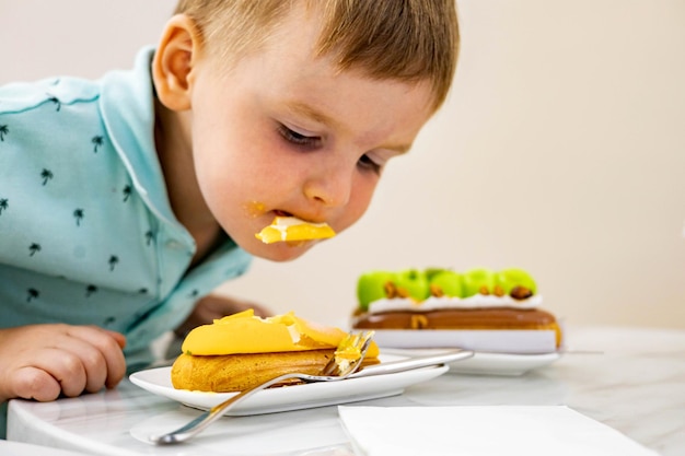 Un petit garçon joyeux mord un café éclair à la mangue avec des gâteaux